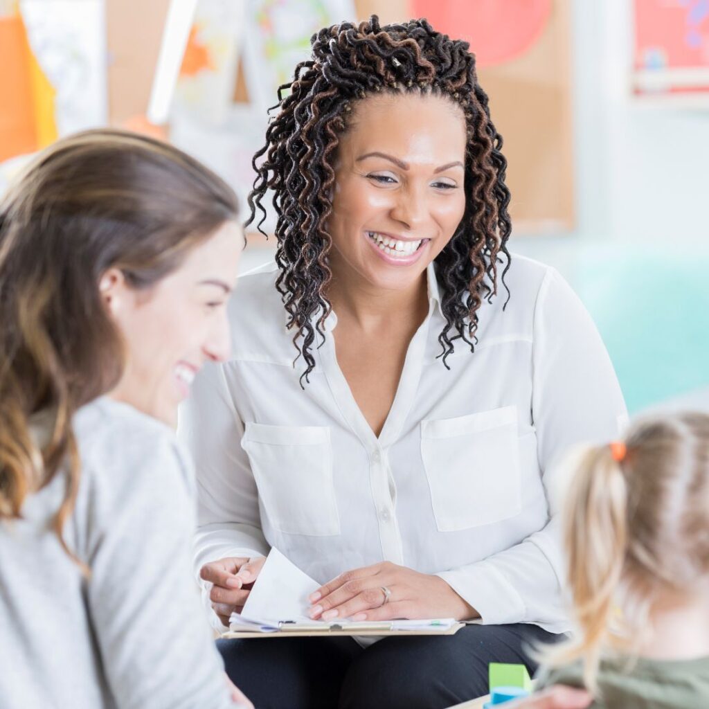 Daycare teacher smiling and talking with mom and daughter