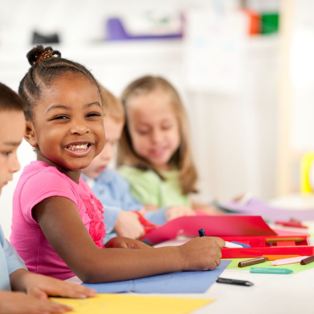 Preschoolers coloring, young girl smiling at camera