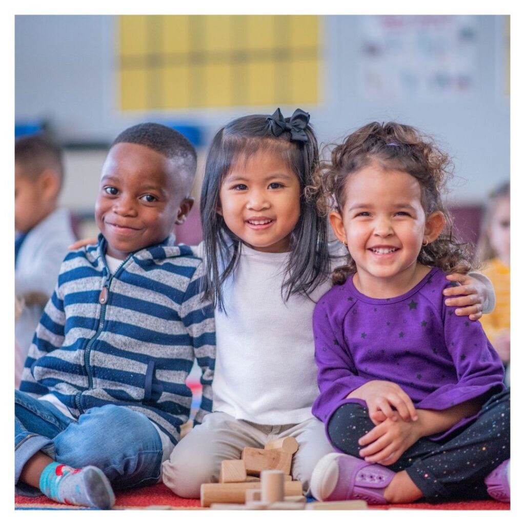 Three smiling children sitting together in a classroom