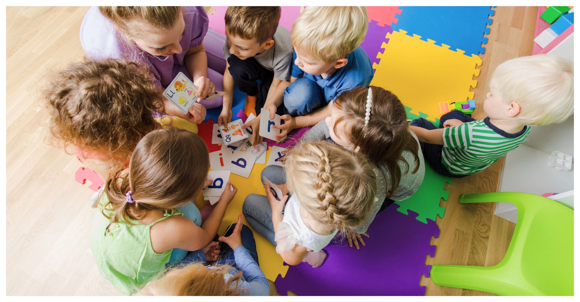 Group of children sitting on colorful foam mats, learning with flashcards