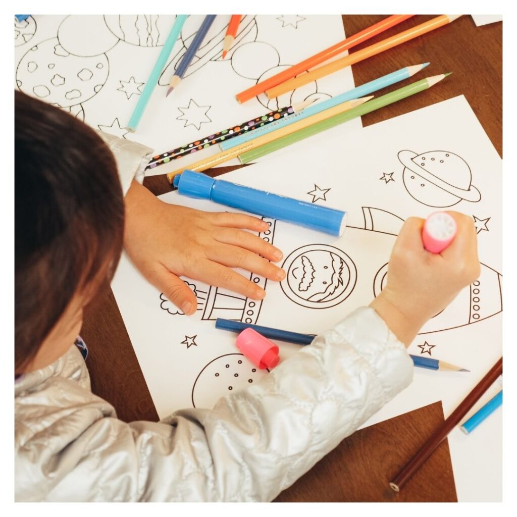 Child coloring space-themed pictures with markers